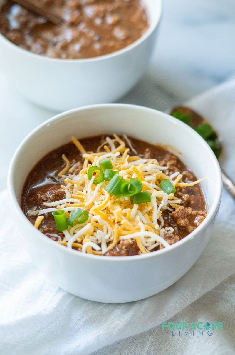 keto chili in a white bowl with cheese and green onions