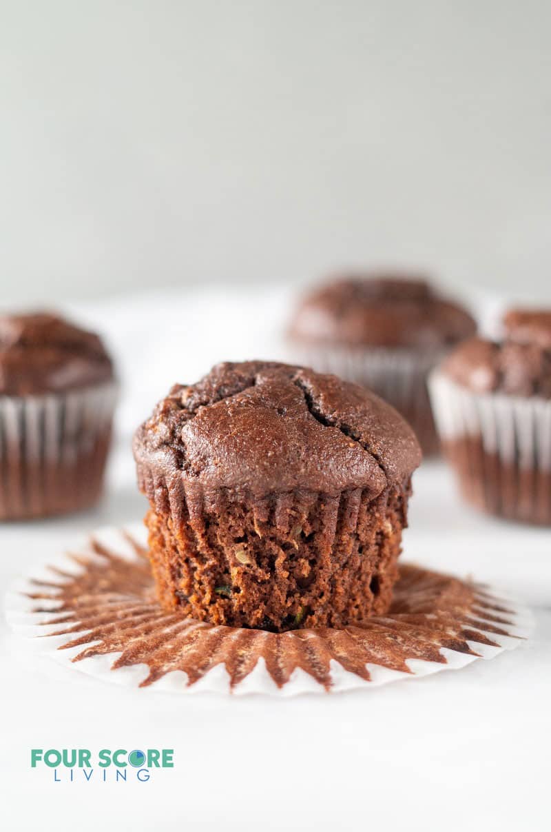 a chocolate muffin sitting on an open cupcake wrapper with several more chocolate muffins in the background.