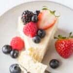 a slice of cheesecake on a plate, topped with fresh berries with a bite being taken.