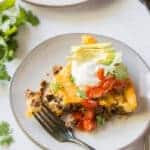 a slice of taco pie on a plate, topped with sour cream, avocoado, tomatoes, and cilantro.