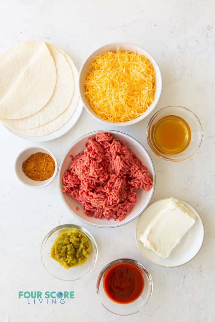 all of the ingredients for taco casserole, each in separate bowls, including ground meat, tortillas, cheese, and seasonings.