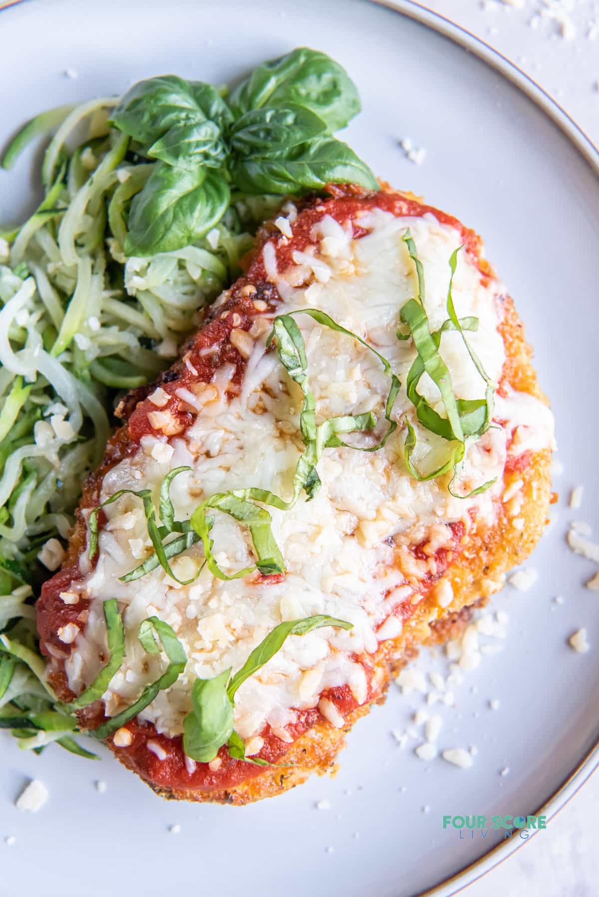 a keto chicken parmesan cutlet garnished with cut basil leaves, with a size of zoodles.