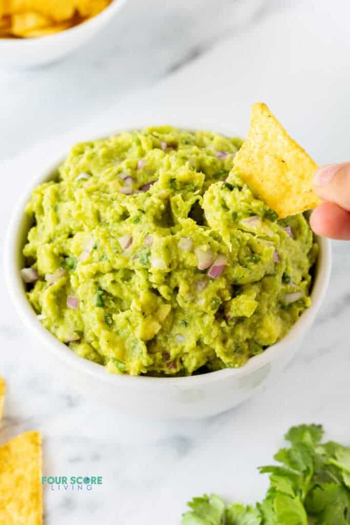 a hand dipping a tortilla chip into 4 ingredient guacamole.