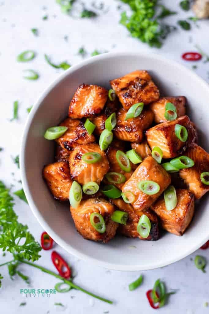 Bowl of honey garlic salmon bites with a chopped scallion garnish.