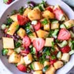 A pineapple salad in a white bowl, with cucumbers, cilantro, red onion and strawberries.