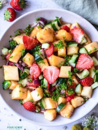 A pineapple salad in a white bowl, with cucumbers, cilantro, red onion and strawberries.