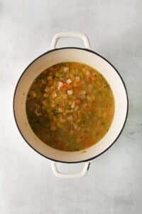 Top view photo of a large stockpot with all the ingredients to make Ham and White Bean Soup, simmering until warmed through.