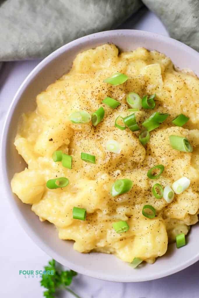 Top view photo of stewed potatoes, garnished with chopped green onions. There is a kitchen towel above the bowl.