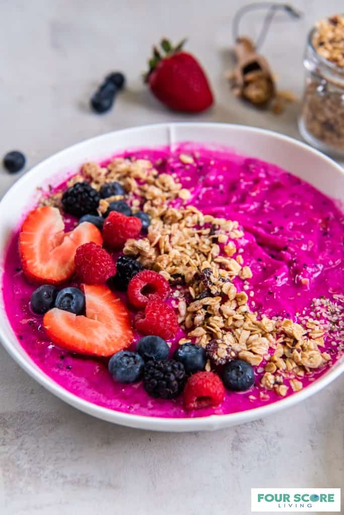 Dragon fruit smoothie bowl in white bowl with raspberries, blackberries, and sliced strawberries layered on top with granola.