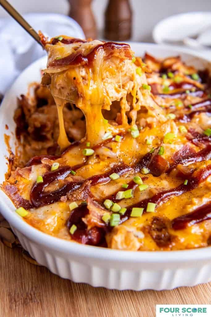 Keto chicken BBQ casserole with a portion being removed with a brass serving utensil and the cheese stretching from the casserole to the utensil.