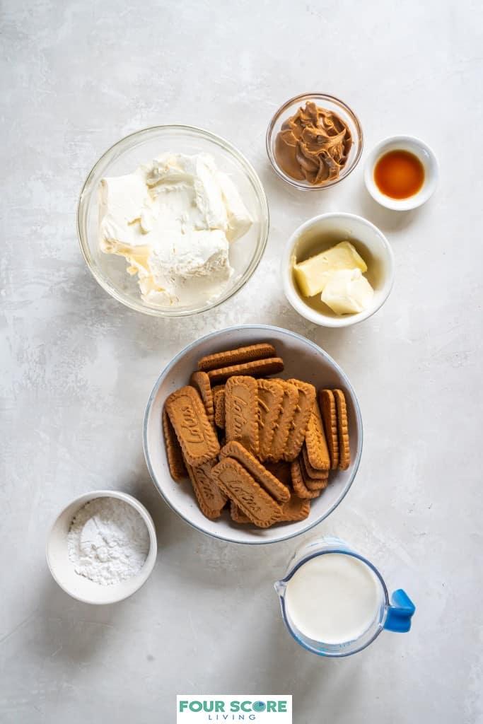 Aerial view of various size bowls holding ingredients to make a Biscoff Cheesecake, including cream cheese, Biscoff cookies, butter, Biscoff spread, heavy whipping cream, vanilla extract and powdered sugar.