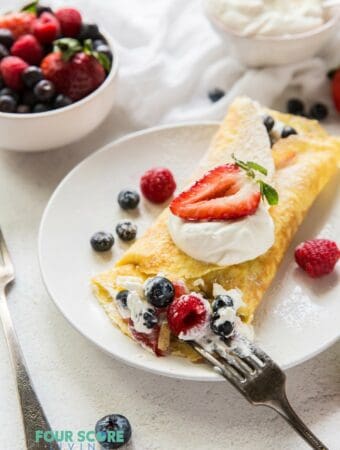 A folded crepe stuffed with cream and mixed berries, being eaten with a fork..