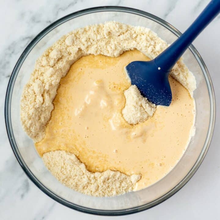 Glass bowl with the wet ingredients being added to the dry and mixed with a spatula.