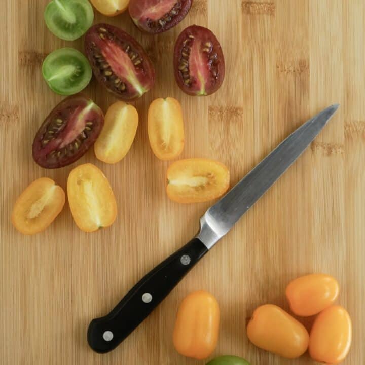 Sliced tomatoes and a sharp knife on a wooden cutting board.