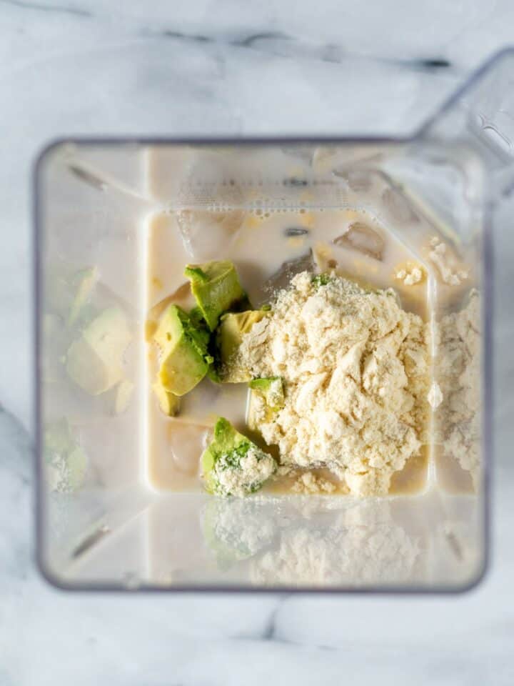 Blender containing cubed avocado, ice, almond milk and protein powder.