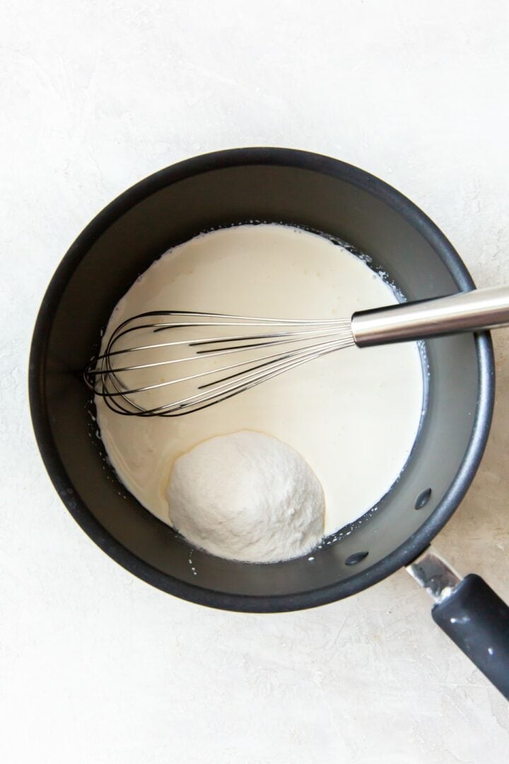 dark metal pot containing heavy cream, sweetener and a silver whisk.
