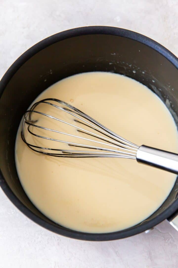 Dark metal pot with heated heavy cream and sweetener and a silver whisk.