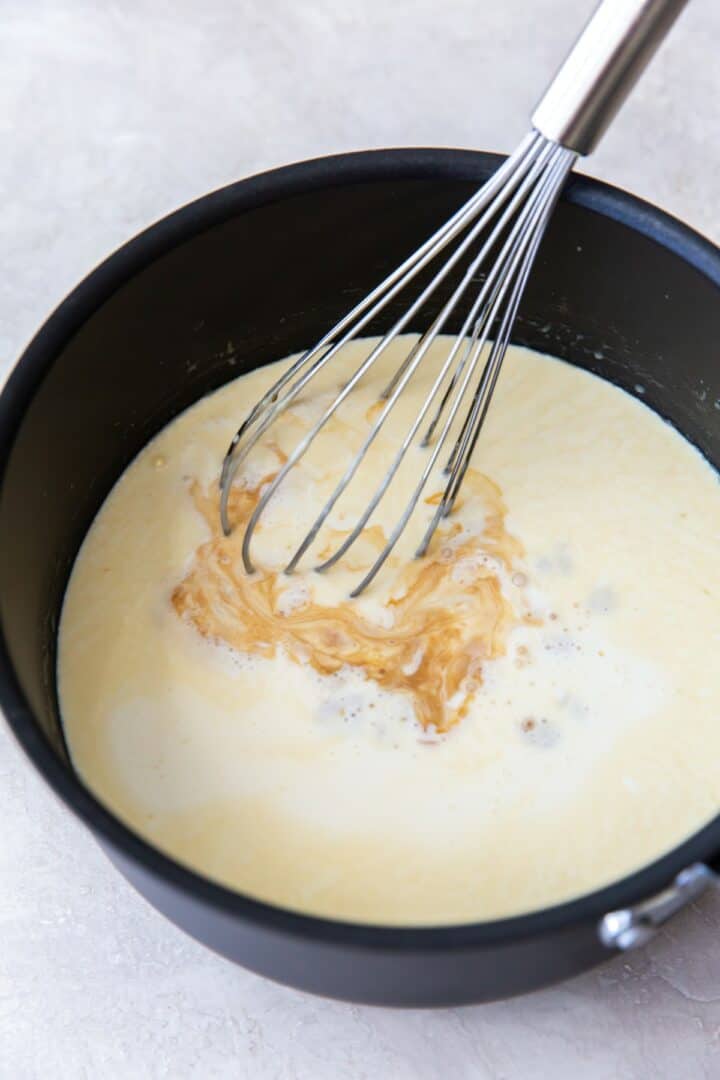 Dark metal pot with a silver whisk. Vanilla extract is being whisked into the sweetened heavy cream.