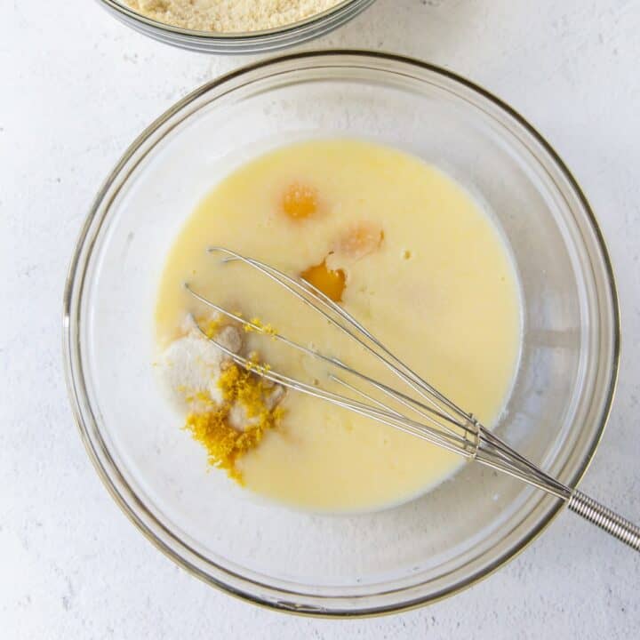 Glass bowl with wet lemon cake ingredients being whisked together.