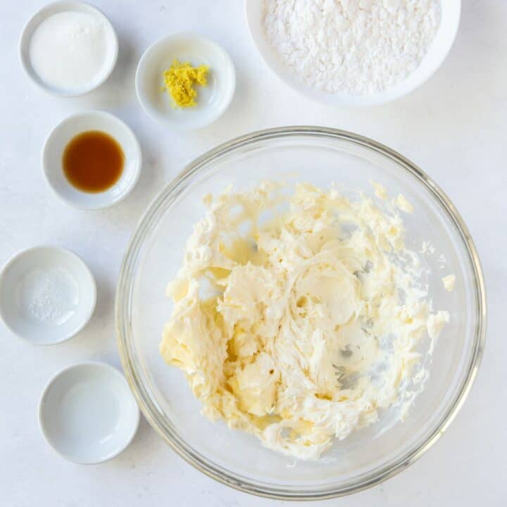 Glass bowl with mixed cream cheese and butter surrounded by individual bowls of the remaining frosting ingredients.