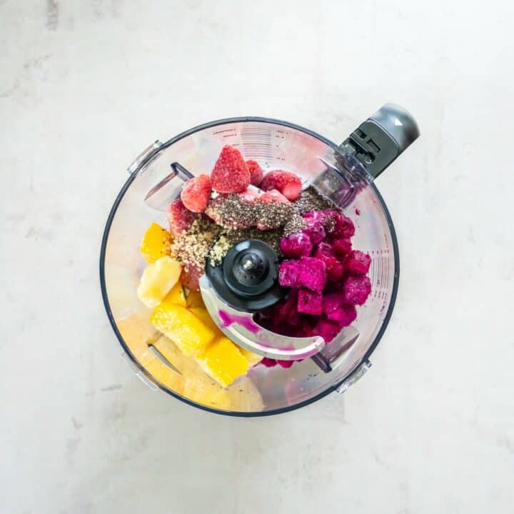 Blender with frozen dragon fruit, mango and strawberries. Chia and hemp seeds are sprinkled on top.