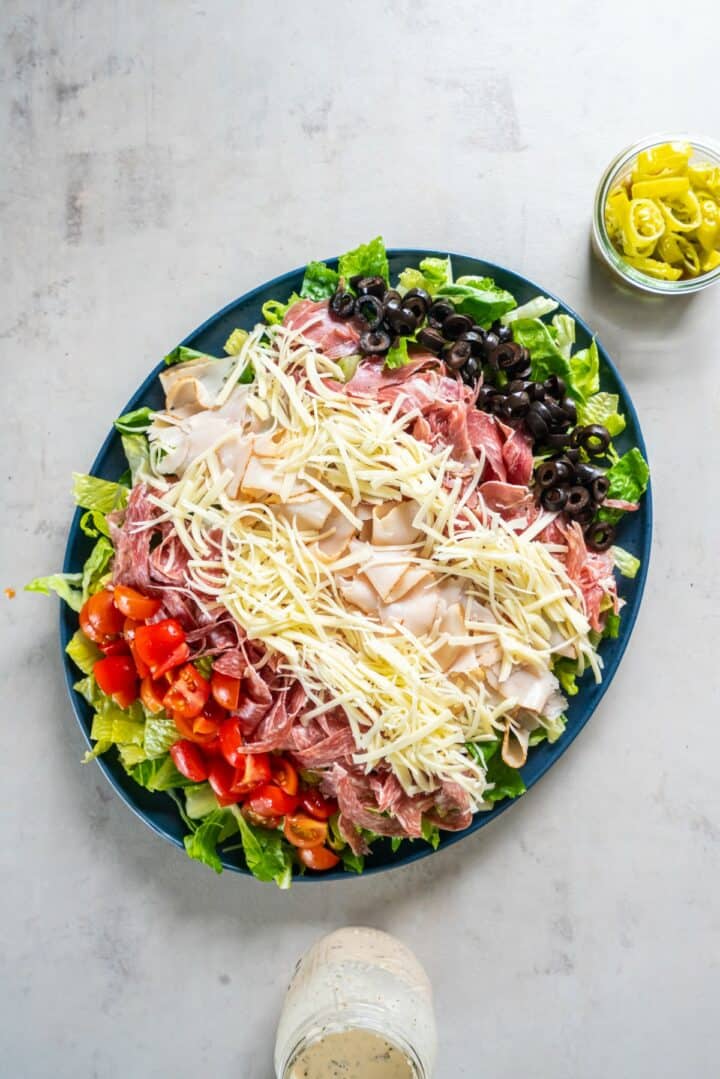 Almost fully assembled grinder salad with banana peppers and dressing still to be put on.