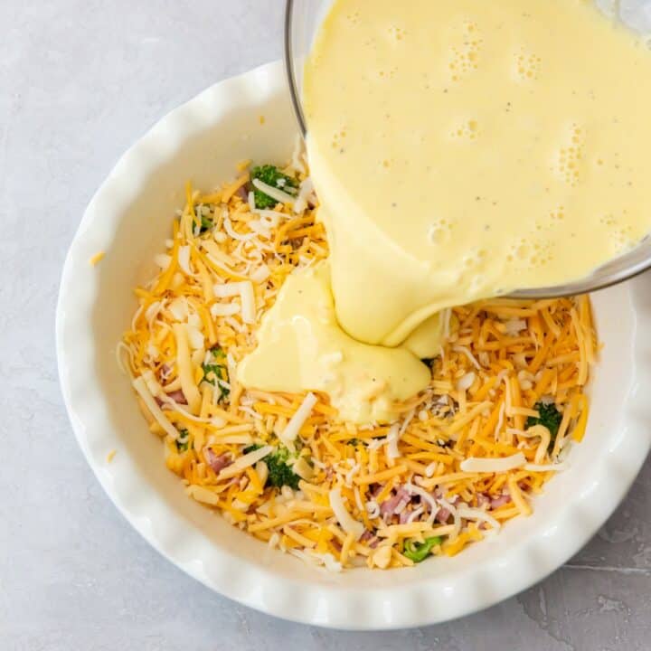 Quiche egg mixture being poured over the shredded cheese and quiche mix ins.