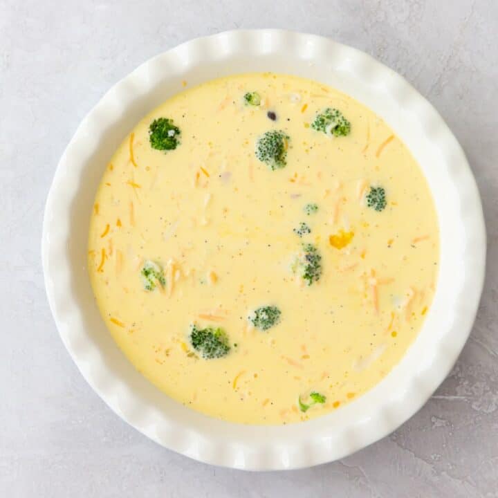 A pie pan filled with all of the mixed ingredients for a crustless keto quiche ready to bake.