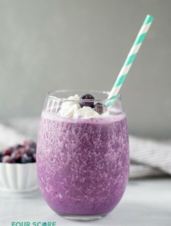 A keto berry smoothie in a glass, topped with whipped cream and blueberries with a straw.