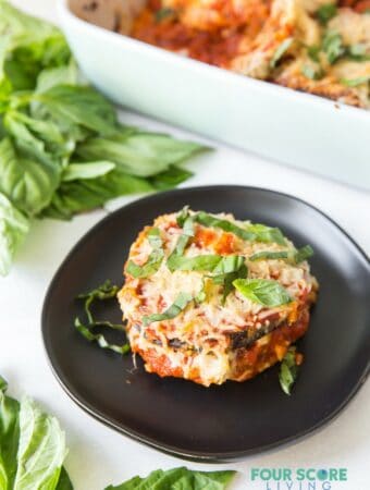 A serving of keto eggplant parmesan on a plate next to a casserole pan.