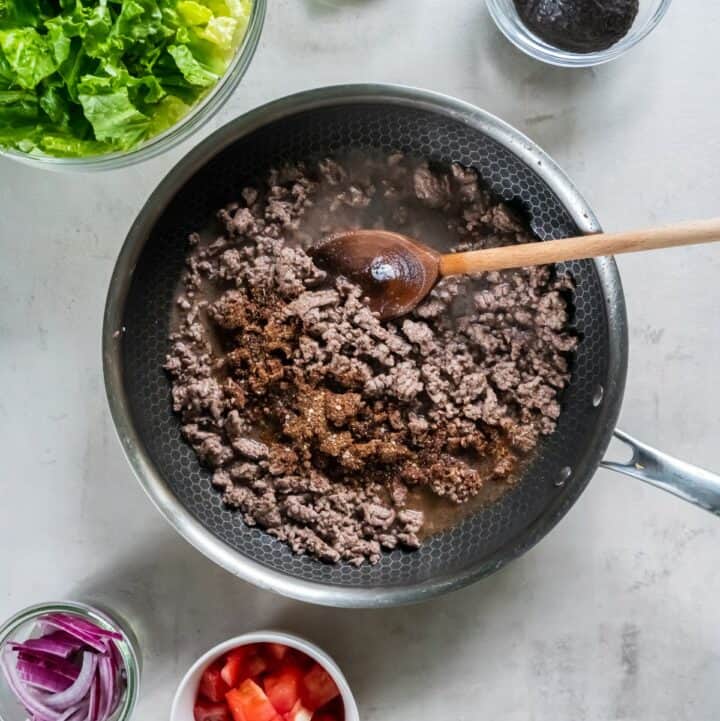 Skillet with browned ground beef with water and taco seasoning being added.