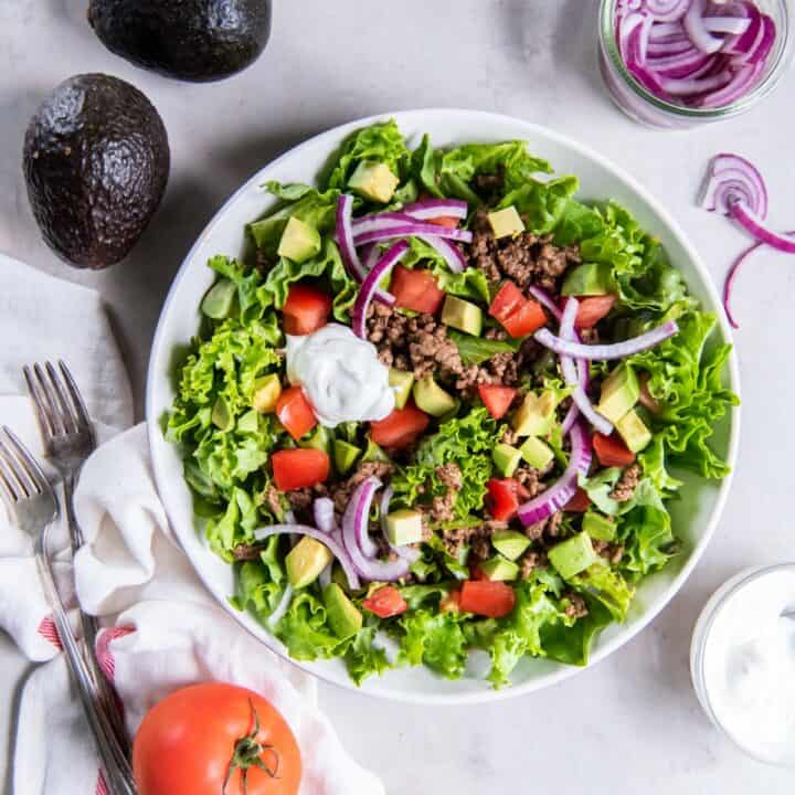 Plate with a finished keto taco salad topped with shredded cheese and a dollop of sour cream.