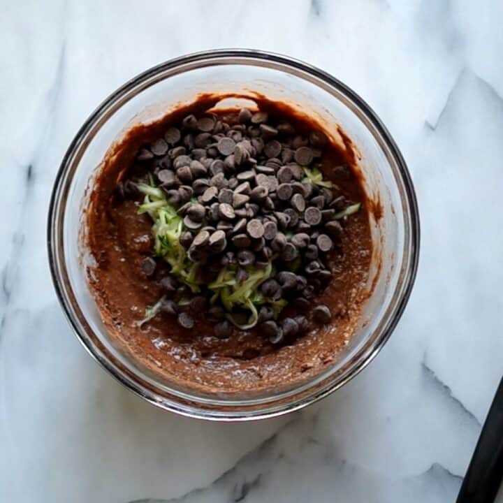 Glass bowl with the shredded zucchini and chocolate chips being added to the other mixed ingredients.
