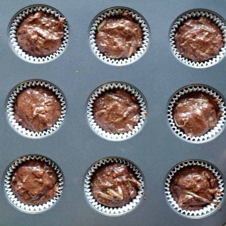 Muffin pan with muffin liners filled with zucchini muffin batter ready to bake.