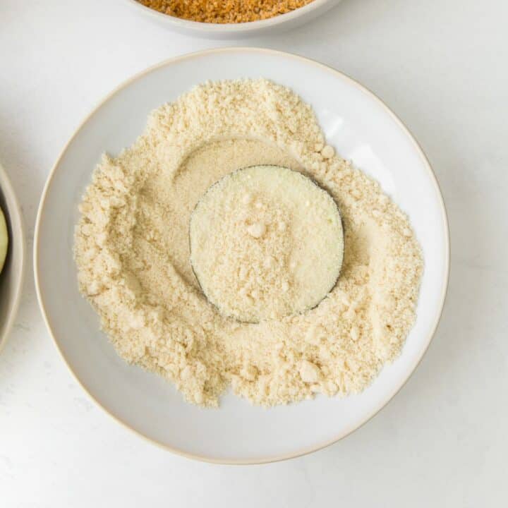 An eggplant round being dipped into almond flour.