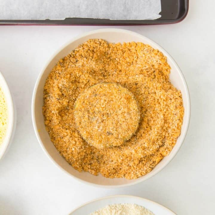 An eggplant round being coated in seasoned pork rinds.