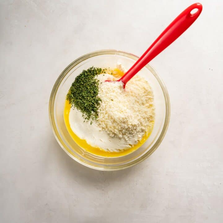 Small glass bowl with egg, ricotta, parmesan and parsley being mixed to make the lasagna filling.