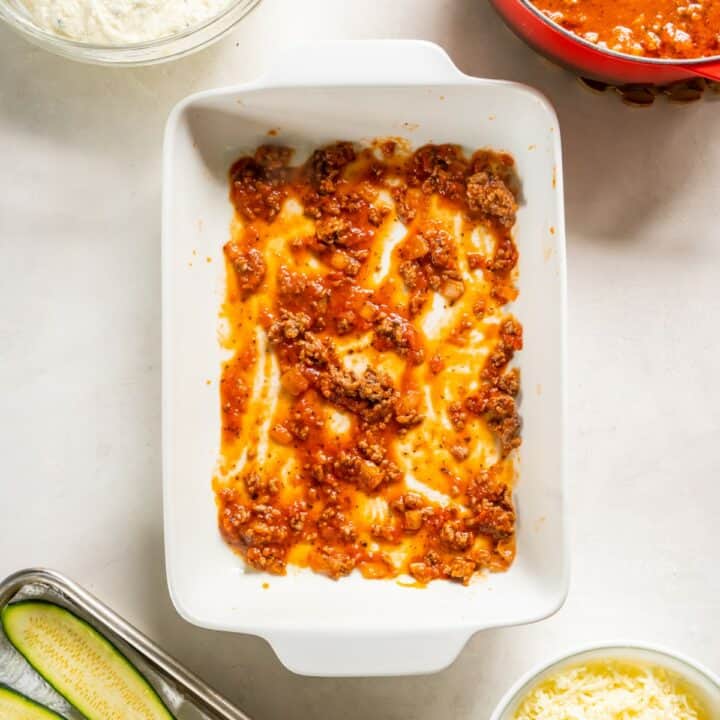 Baking dish with the light layer of meat sauce spread at the bottom.
