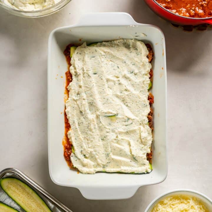 Baking dish with one third of the ricotta filling being spread on top of the zucchini slices.
