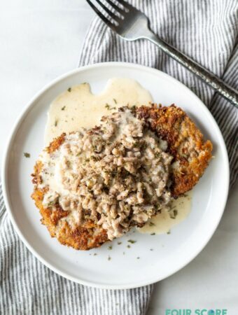 Chicken fried steak with sausage gravy on a round plate next to a fork and napkin.