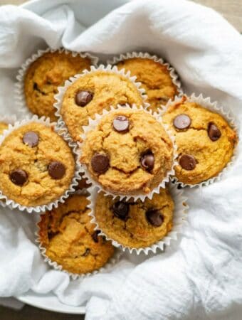 low carb pumpkin muffins with chocolate chips on a white dish towel in a bowl.