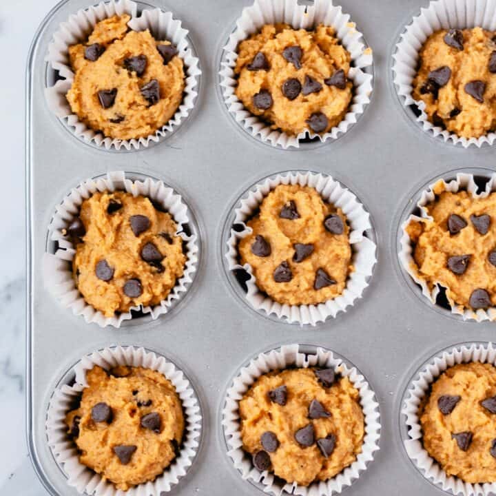 Nine unbaked pumpkin muffins topped with chocolate chips in a muffin pan.