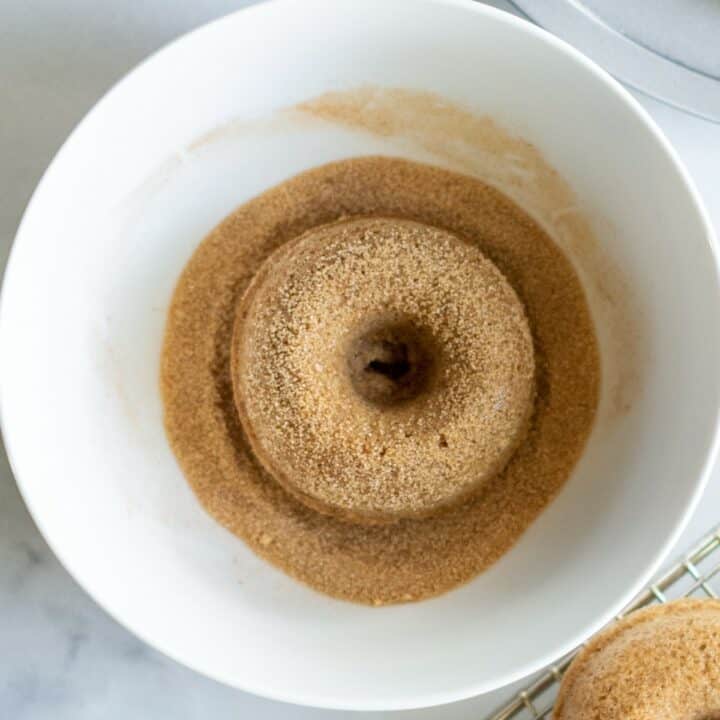 A keto donut being dipped in a bowl of cinnamon sugar.